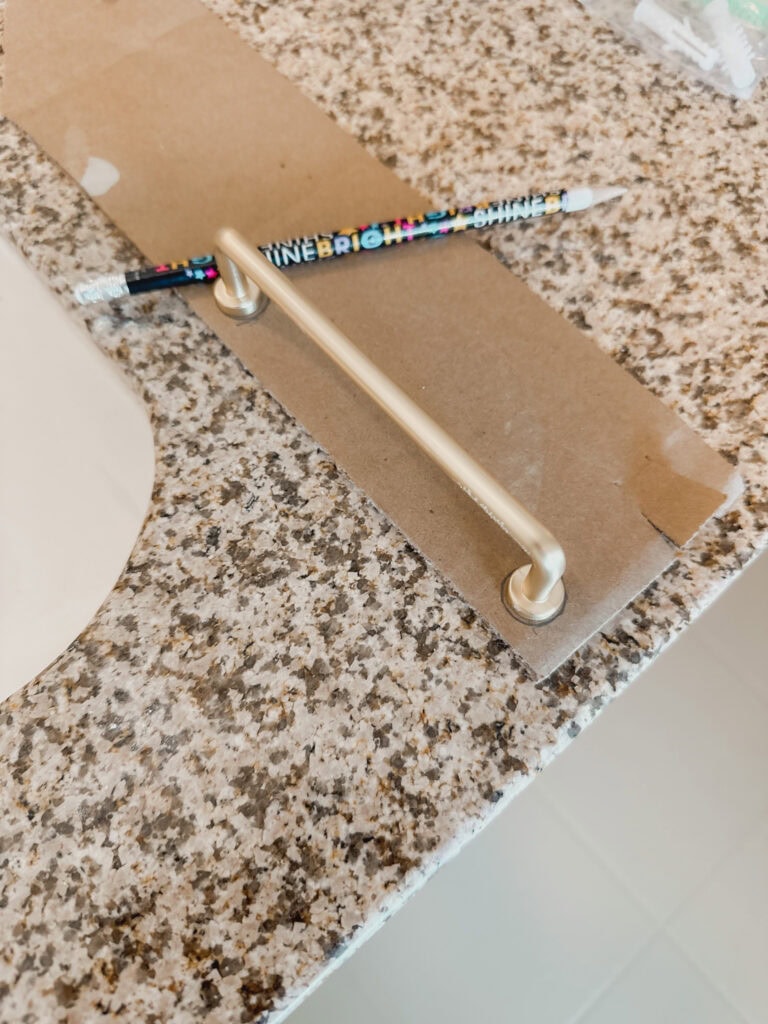 brass handle on cardboard with a pencil to demonstrate tracing the hardware to make your template.